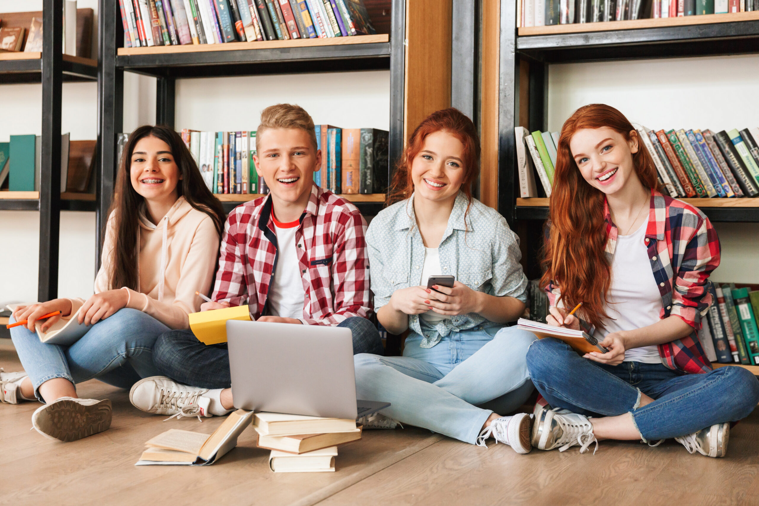 Four young adults sitting on the floor of a library.