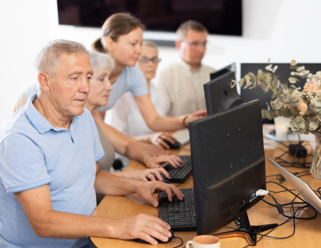 A group of learners sitting at desk with open laptops. The tutor is standing behind pointing to something on a screen.