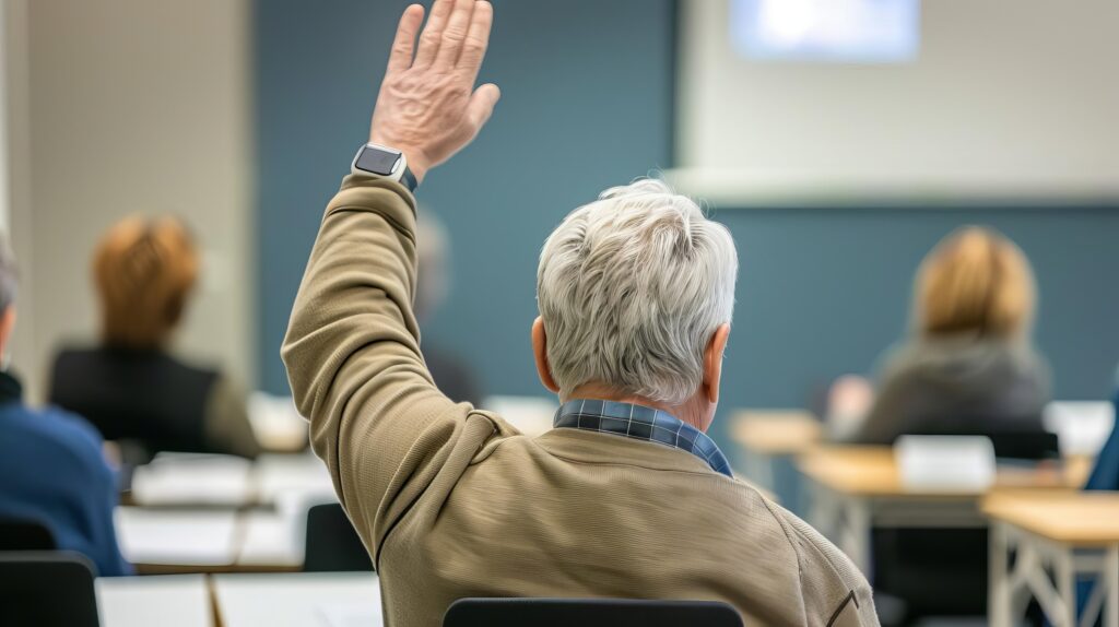 Back view of an older student raising his hand to answer a question in a classroom setting