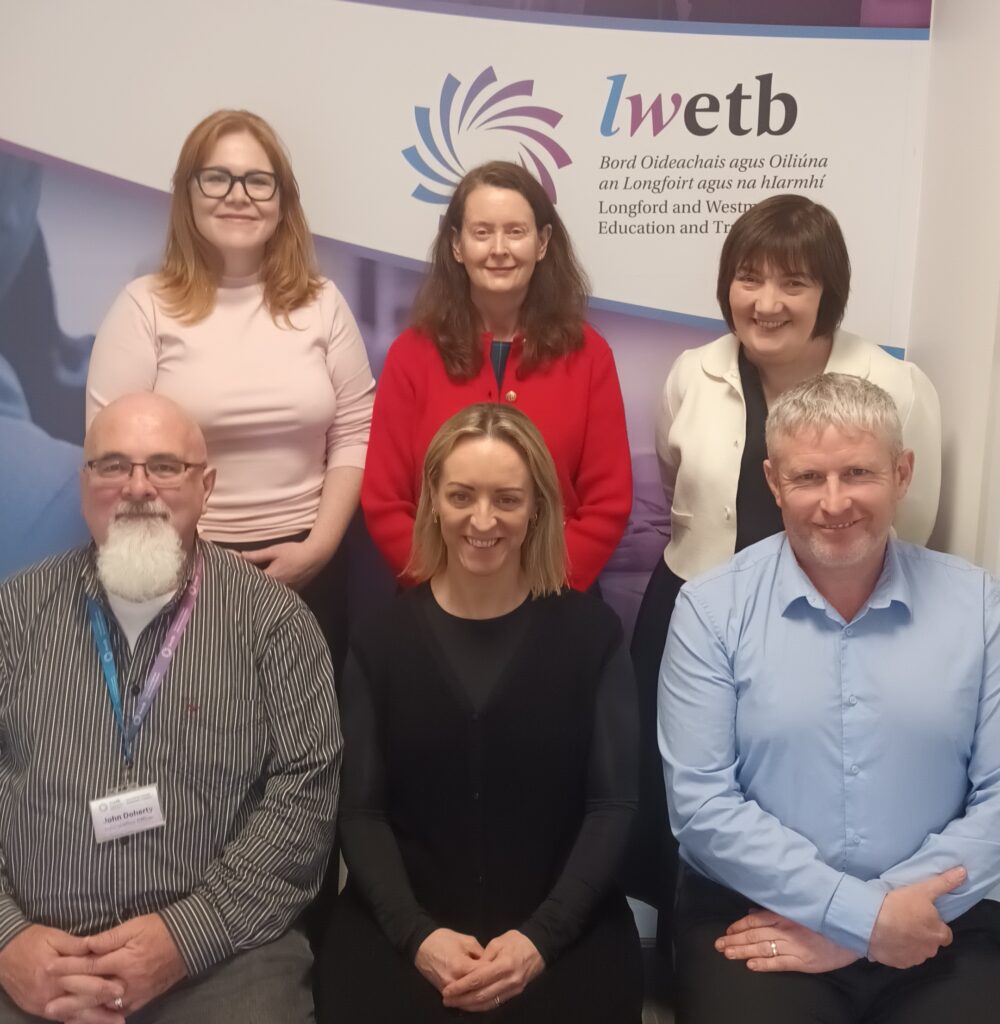 Six adults, three seated and three standing, pose in front of an LWETB FET Guidance and Information Service banner. The group consists of three men and three women, all facing the camera and smiling.